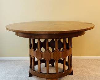 A very collectible Mid-Century Modern wooden round top expandable table with 3 additional leaves and support legs, and a distinct sculptural base design