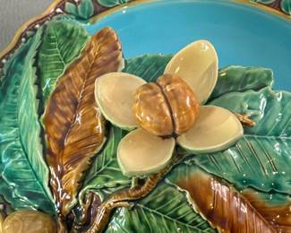 Closeup of the stunning antique Minton Majolica chestnut server, round in shape with low pedestal base, attached half covered dome lid modeled as leaves of varying shades of green and brown, with applied spreading nut shell holding raised tan color nut within it, scalloped edge in gold with green leaf/white dot flower design ending in rolled grip handle, turquoise liner, 11-1/2" diameter by 7” H, impressed maker's marks for the Minton pottery and a pattern number, '694'. Circa 1860s-1880s.