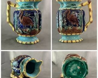 An American majolica pitcher circa 1880-90; heavy cast, molded pitcher with raised cranes painted brown against a cobalt blue background against a low brick wall; four borders of yellow bamboo, top/bottom rim and end handle also of bamboo design.