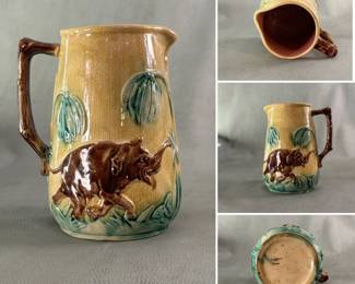 Antique American majolica pitcher, circa 1885, brightly glazed with raised hand-colored brown elephants on a yellow background amidst green palm-like trees, with a branch-shaped handle and lavender glaze inside.