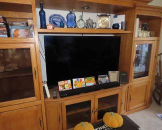 Large three piec entertainment center, Tv, sound bar, DVDs, candles, colored bottles. World mantle clock