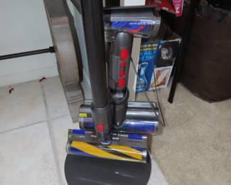 Dyson stick vacuum with charging stand and attachments.