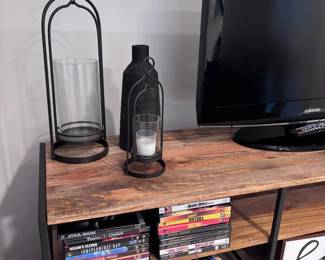Wood TV console with DVDs, decorative candle lantern, glass bottle