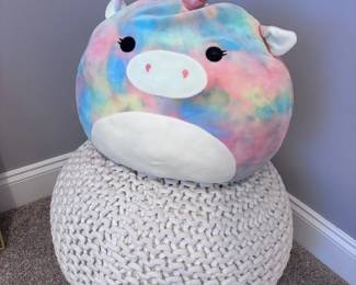Large Squishmallow unicorn plush on white knit pouf ottoman