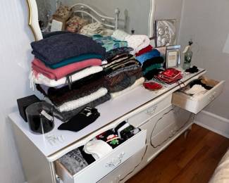Vintage style vanity with mirror full of clothing on top and in the drawers