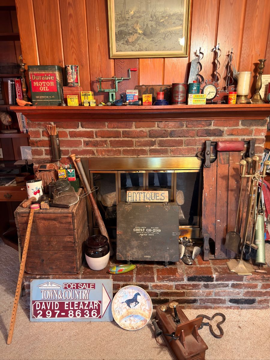 Antique fireplace display with vintage oil cans, tins, brass tools, and signs