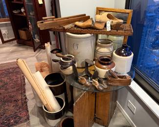 Circular Glass Display Top: A thick, tempered clear glass roundsheet Price $99 | Wooden Crate Base: A weathered wooden shipping crate used as a rustic pedestal,$75.00 | Tan 6-gallon ceramic Vessel housed into the crate $495 | Two-Tone Handled Glazed Pot: A wide-mouthed ceramic vessel with a deep chocolate-brown glazed rim and handles $55 | Miniature Wooden Shoe Lasts: A pair of small, hand-carved vintage wooden shoe molds with weathered patina Price: $50.00 (Pair) | (on the floor) Antique Brown ceramic unglazed Pot $125