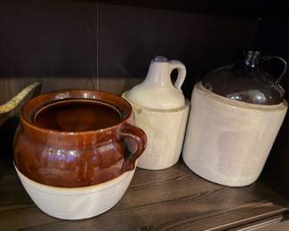 Two-Tone Handled Bean Pot: round ceramic crock brown glazed top and a maturing a deep chocolate with cream base, complete with a sturdy side handle. Price: $45.00  | Antique White Ceramic Jug: A classic small-mouth stoneware jug with a finger-loop handle and a distressed white-to-grey finish. Price: $35.00 |   Large Two-Tone Storage Jug: substantial stoneware vessel with a dark brown glazed upper shoulders and neck, contrasting against a heavy cream-colored body. Price: $65.00