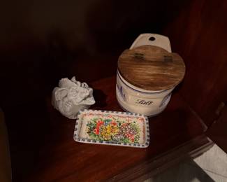 White Ceramic Gargoyle Bust: A small, detailed gothic-style gargoyle sculpture with an unglazed, matte finish. Price: $20.00 | Hand-Painted Floral Rectangular Dish: A decorative ceramic tray featuring vibrant, multi-colored floral artwork and a blue-and-white dotted border. Price: $22.00 | Vintage Ceramic Salt Cellar: A white stoneware crock labeled "Salt" in blue script, featuring a hinged wooden lid and a pre-drilled hole for wall mounting. Price: $35.00  