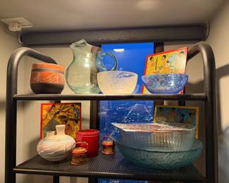 Far Top Right, Brown Ceramic Etched Bowl: reddish-brown ceramic bowl with etched patterns and a figure, in a Mayan style. Price: $30 | Large Clear Glass  Serving Pitcher  $25 | Etched Frosted Glass Bowl $67 | Textured Blue Glass Bowl $33 | Small Folk Art Prints (Behind bowls) $15 each | White Ceramic Vase $45 | Large Glass Ribbed lined Bowl with Papers $49 |   Nashji surface pattern bow $50   