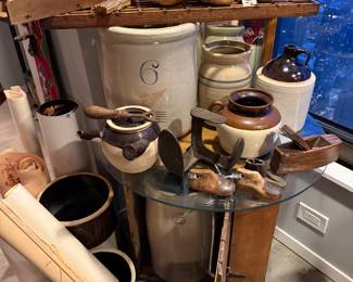 Circular Glass Display Top: A thick, tempered clear glass roundsheet Price $99 | Wooden Crate Base: A weathered wooden shipping crate used as a rustic pedestal,$75.00 | Tan 6-gallon ceramic Vessel housed into the crate $495 | Two-Tone Handled Glazed Pot: A wide-mouthed ceramic vessel with a deep chocolate-brown glazed rim and handles $55 | Miniature Wooden Shoe Lasts: A pair of small, hand-carved vintage wooden shoe molds with weathered patina Price: $50.00 (Pair) | (on the floor) Antique Brown ceramic unglazed Pot $125