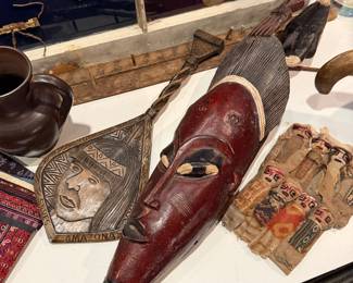 Red hand-carved African tribal mask, identified as a Guro or Baule mask from the Ivory Coast or Ghana region, Price: $480, Chancay burial dolls from Peru $45, To the left of red mask is a Wooden wall plaque South America based with "Amazonas" markin g $98  
