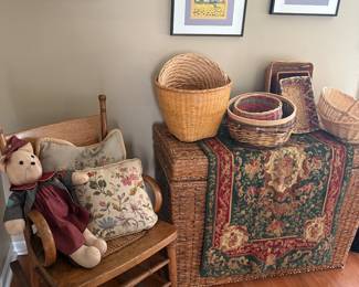 Antique wood rocking chair, large wicker storage chest, needlepoint runner and pillows, baskets, and framed lithographs