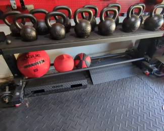 Lot 43:Set of Rogue kettle weights on rolling stand ranging from 25 lb to 70 lb. Includes pair of rogue diamond plate, metal ramps underneath and balls. All for your bid