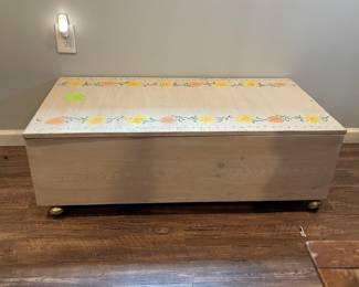 D64 - $30. Wooden Toy Storage Box on Wheels. Measures 44" wide x 23.25" deep x 14.5" tall. Stenciled floral top. Does NOT have safety hardware!