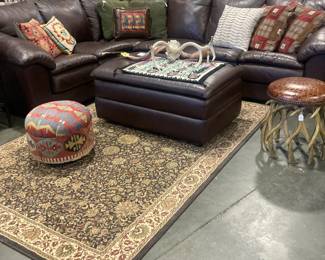 Brown leather sectional with ottoman, Antler stool with leather seat, 4 x 6 area rug, throw pillows, books in background