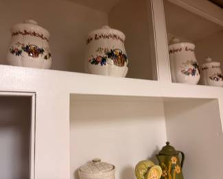 Ceramic floral canister set on kitchen shelf, green glass bottle