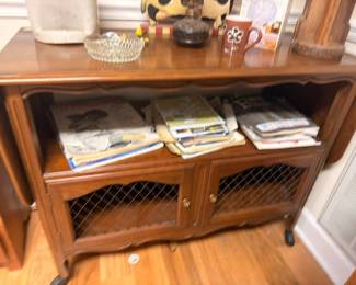 Wooden TV stand console with open shelf, books, magazines, and collectibles