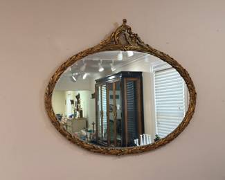 Antique oval wall mirror with ornate gold gilt frame and decorative crest