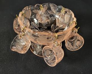 Lot # : 10 - Miniature Pink Depression Glass Set Miniature pink depression glass punch bowl measuring 4.5´´ x 3.5´´ tall with six punch cups measuring 1´´ tall, featuring a strawberry pattern. The bowl has a scalloped rim and raised details, and the cups showcase matching etched designs. Include s metal cup hooks for display.