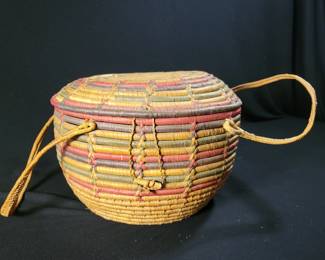 Lot # : 2 - Hand Woven Coiled Basket of Natural Fibers Handmade Coiled basket constructed with natural fibers, featuring vibrant multicolored designs. Includes a lid and two leather straps. Estimated dimensions 10.5 inches tall and 7.75 inches wide. Suitable for decorative or functional use