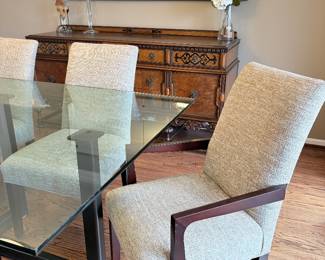 1" glass rectangular dining table with black metal base shown with wood and upholstered chairs in front of a Jacobean sideboard and large mirror