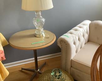 Round table with metal legs, glass lamp and shade, “poof” footstool