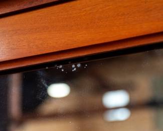 A large mahogany sideboard with an attached mirror by Aldis & Leggott, cabinet makers from Hull. The piece features four drawers, two side cabinets with pull-out shelves, and a specialized interior section for bottle storage. Decorative carvings on the legs and facade, as well as brass drawer pulls, highlight the craftsmanship. Dovetail joinery is observed on the drawers, indicating quality construction. The mirror shows minor silvering loss, and the wooden structure displays some signs of wear consistent with age, including small scratches and woodworm holes. Stamped “Aldis & Leggott, 17 Paragon Street, Hull”. This stunning sideboard measures 77” H X 78” W x 26” D.