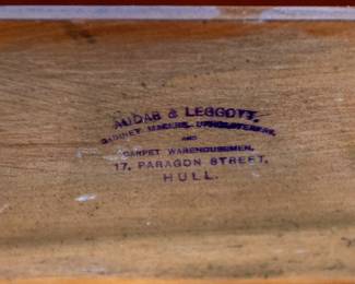 A large mahogany sideboard with an attached mirror by Aldis & Leggott, cabinet makers from Hull. The piece features four drawers, two side cabinets with pull-out shelves, and a specialized interior section for bottle storage. Decorative carvings on the legs and facade, as well as brass drawer pulls, highlight the craftsmanship. Dovetail joinery is observed on the drawers, indicating quality construction. The mirror shows minor silvering loss, and the wooden structure displays some signs of wear consistent with age, including small scratches and woodworm holes. Stamped “Aldis & Leggott, 17 Paragon Street, Hull”. This stunning sideboard measures 77” H X 78” W x 26” D.