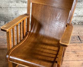 This lot features an antique Mission Arts and Crafts style rocking chair, with a curved back and in good sturdy condition. This chair measures, 33” H x 25” W x 30” D.