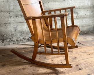 This lot features an antique Mission Arts and Crafts style rocking chair, with a curved back and in good sturdy condition. This chair measures, 33” H x 25” W x 30” D.