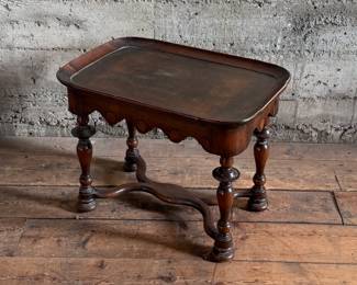 This lot features a William and Mary style walnut tea or side table, often recognized by its turned legs, scalloped apron, and stretcher base that measures, 18” H x 24” W x 16” D.