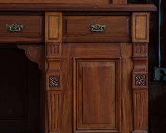 A large mahogany sideboard with an attached mirror by Aldis & Leggott, cabinet makers from Hull. The piece features four drawers, two side cabinets with pull-out shelves, and a specialized interior section for bottle storage. Decorative carvings on the legs and facade, as well as brass drawer pulls, highlight the craftsmanship. Dovetail joinery is observed on the drawers, indicating quality construction. The mirror shows minor silvering loss, and the wooden structure displays some signs of wear consistent with age, including small scratches and woodworm holes. Stamped “Aldis & Leggott, 17 Paragon Street, Hull”. This stunning sideboard measures 77” H X 78” W x 26” D.
