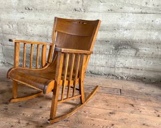 This lot features an antique Mission Arts and Crafts style rocking chair, with a curved back and in good sturdy condition. This chair measures, 33” H x 25” W x 30” D.
