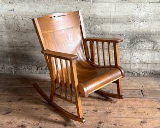 This lot features an antique Mission Arts and Crafts style rocking chair, with a curved back and in good sturdy condition. This chair measures, 33” H x 25” W x 30” D.