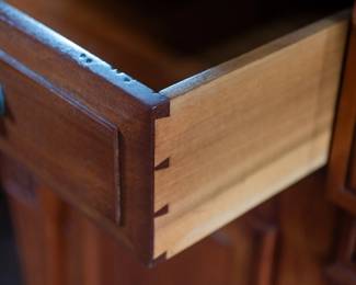 A large mahogany sideboard with an attached mirror by Aldis & Leggott, cabinet makers from Hull. The piece features four drawers, two side cabinets with pull-out shelves, and a specialized interior section for bottle storage. Decorative carvings on the legs and facade, as well as brass drawer pulls, highlight the craftsmanship. Dovetail joinery is observed on the drawers, indicating quality construction. The mirror shows minor silvering loss, and the wooden structure displays some signs of wear consistent with age, including small scratches and woodworm holes. Stamped “Aldis & Leggott, 17 Paragon Street, Hull”. This stunning sideboard measures 77” H X 78” W x 26” D.