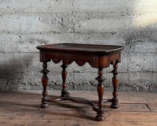 This lot features a William and Mary style walnut tea or side table, often recognized by its turned legs, scalloped apron, and stretcher base that measures, 18” H x 24” W x 16” D.