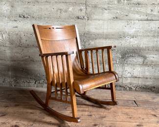 This lot features an antique Mission Arts and Crafts style rocking chair, with a curved back and in good sturdy condition. This chair measures, 33” H x 25” W x 30” D.