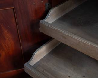A large mahogany sideboard with an attached mirror by Aldis & Leggott, cabinet makers from Hull. The piece features four drawers, two side cabinets with pull-out shelves, and a specialized interior section for bottle storage. Decorative carvings on the legs and facade, as well as brass drawer pulls, highlight the craftsmanship. Dovetail joinery is observed on the drawers, indicating quality construction. The mirror shows minor silvering loss, and the wooden structure displays some signs of wear consistent with age, including small scratches and woodworm holes. Stamped “Aldis & Leggott, 17 Paragon Street, Hull”. This stunning sideboard measures 77” H X 78” W x 26” D.
