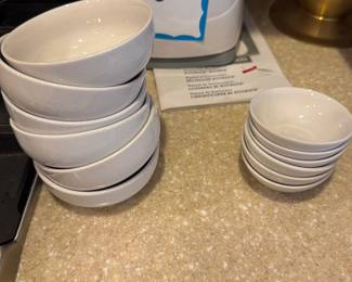 Set of white ceramic bowls in two sizes, including larger soup/cereal bowls and smaller condiment or dipping bowls.