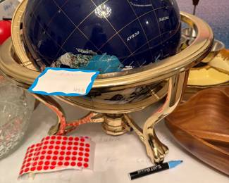 Decorative illuminated navy-blue world globe featuring gold latitude and longitude lines with labeled oceans and continents. Mounted in a polished brass-tone stand with classic curved legs and rotating ring frame, allowing the globe to tilt and spin. Elegant desk or bar décor piece, great for an office, study, or library display.  Good condition with normal light wear.