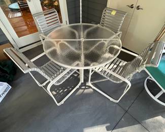 C28 - $350. Woodard Furniture Glass Top Table & 4 Vinyl Strap Chairs. Measures 47.5" round x 28" tall. Chairs are 23.5" x 25.5" x 36" tall. Has been used on a screened in porch - a few very minor rust spots