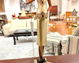 A stylized Art Deco–style sculpture of a fashionable woman in a geometric gold dress, likely inspired by works from designers such as Chiparus or Erte, standing on a stepped base and holding a dangling chain accessory.