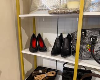 Metallic silver tote and sequined clutch are displayed beside black pointed-toe heels with red interiors and black ankle boots.