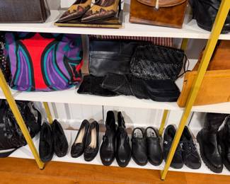 Colorful patterned tote sits beside several black leather clutches and woven bags (including a Fendi monogram clutch), with multiple pairs of black loafers, ankle boots, and sneakers arranged below.