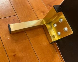 Modern brushed brass metal furniture leg with black floor protectors.