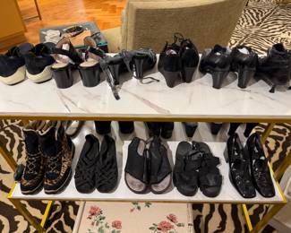 Shoe display table showing multiple pairs of heels, wedges, sandals, and casual footwear in black and neutral tones.