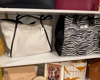 Assorted handbags and accessories including a cream leather Coach tote with black trim, zebra-print Piero Rosetti tote bag, red structured handbag, tan leather handbag, beige envelope clutch, patterned fabric tote, and a framed religious icon.