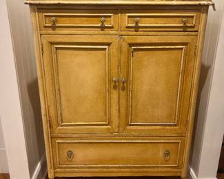 Vintage distressed cream wood cabinet with two drawers, double doors, lower drawer, and caster feet.
