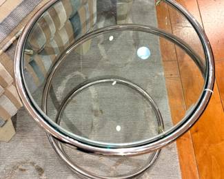 A modern chrome cantilever side table with a circular glass top and continuous tubular steel base, in the style of designs by Ludwig Mies van der Rohe and Marcel Breuer, circa 1970s–1990s.